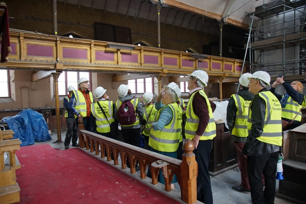 Crowd of visitors in yellow hi viz vests looking up at the organ gallery