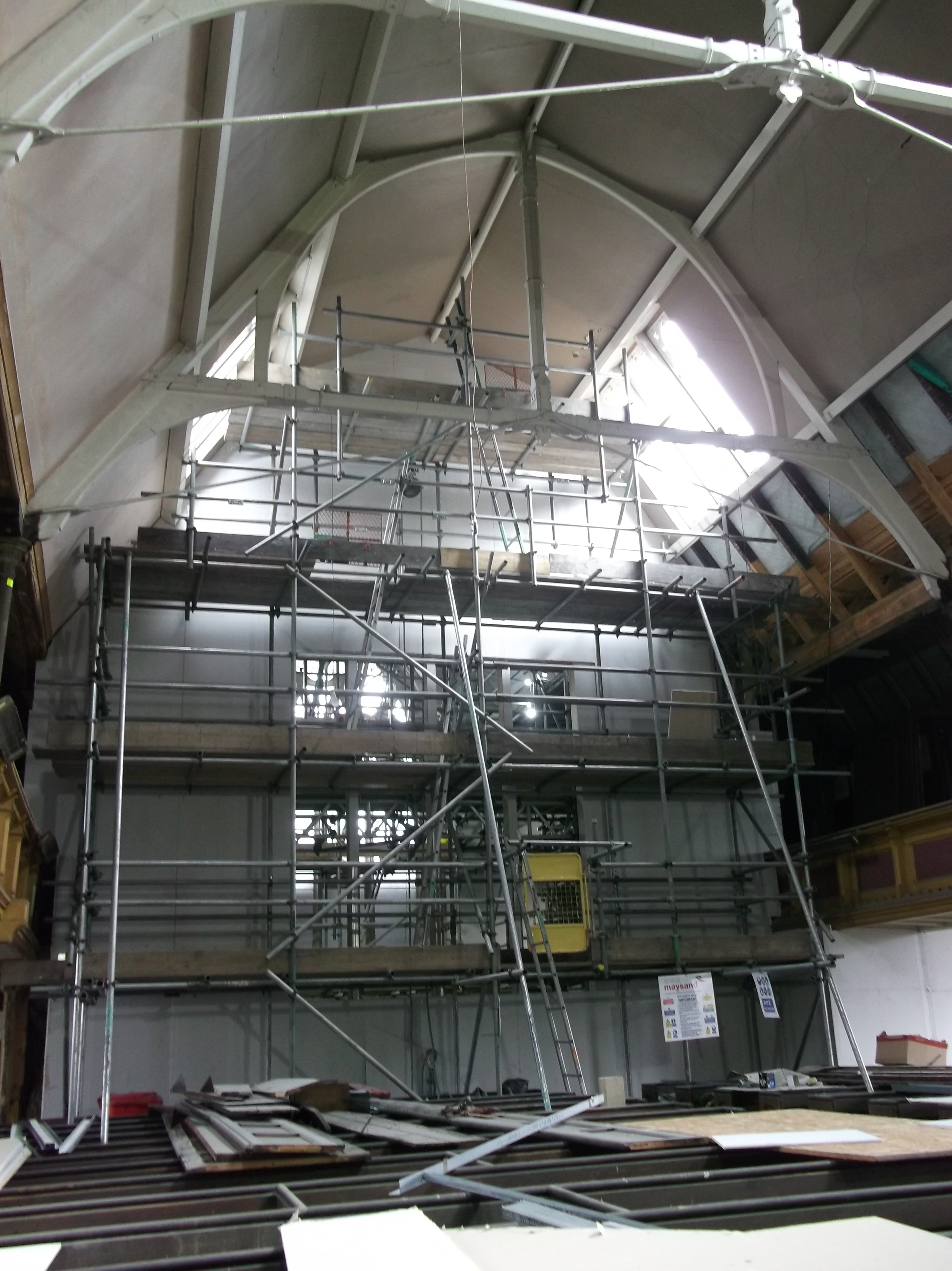 Scaffolding in front of a plastered wall with a view of the east window tracery in the middle