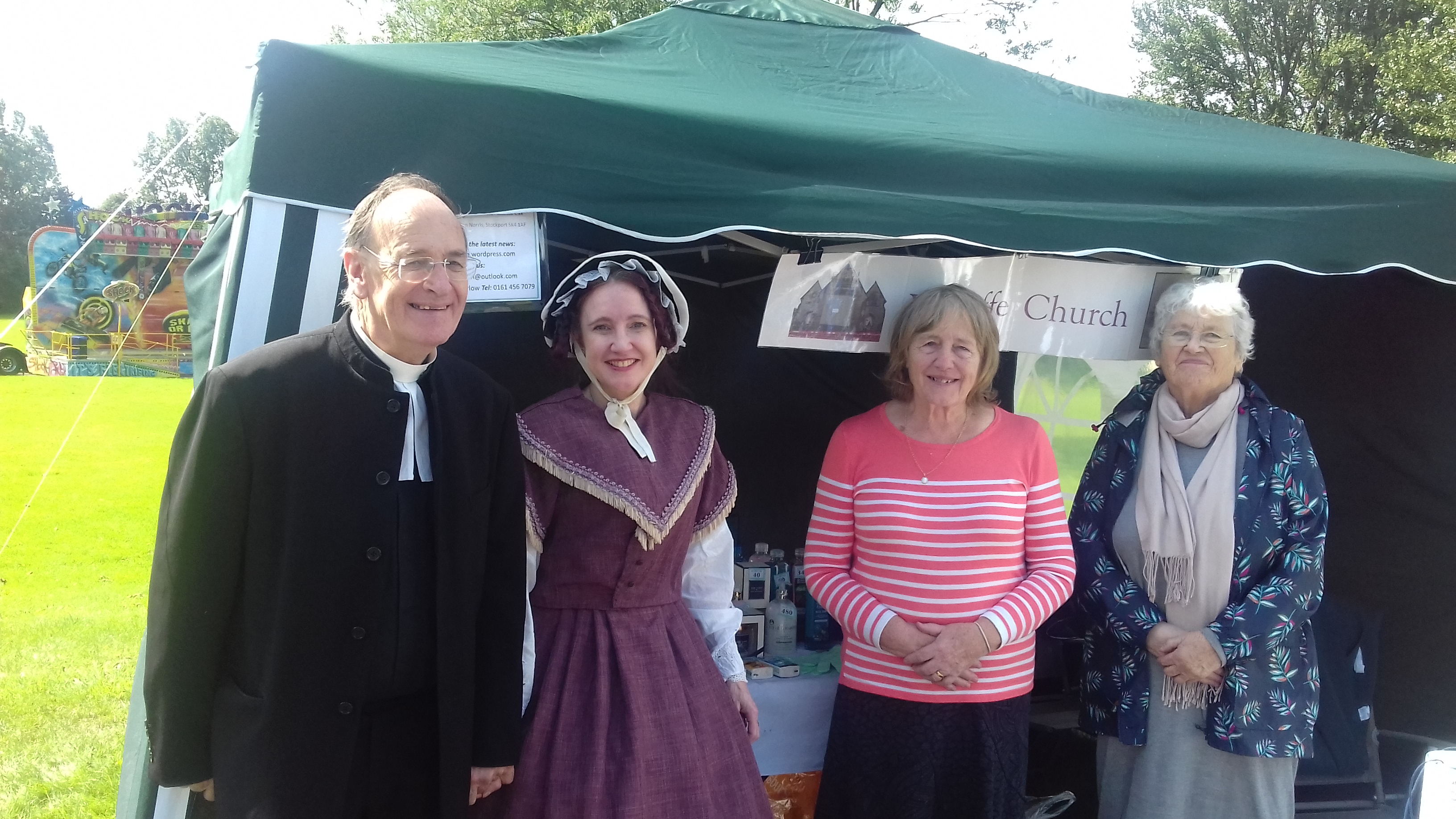 Four volunteers smile in front of a gazebo with a Wycliffe Church sign on. 