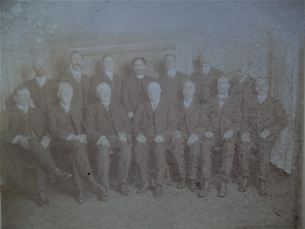 A faded image of 7 standing and 7 seated men of Wycliffe