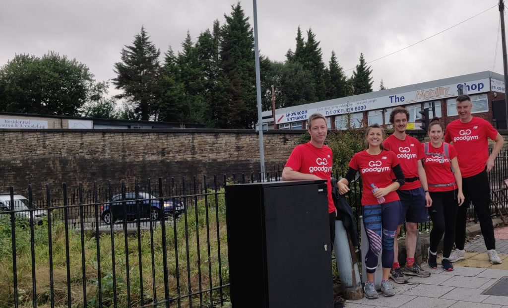 Five members of the GoodGym Stockport wearing their branded red tee shirts stand in front of the cleared garden on the corner of Georges Road and Wellington Road North