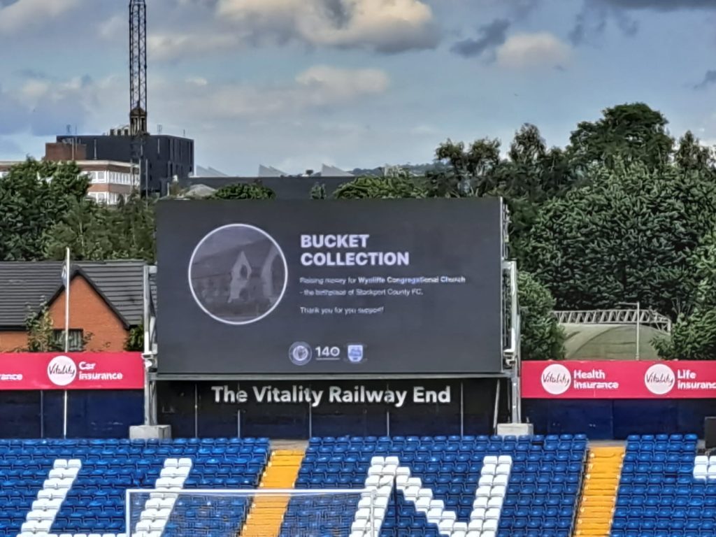 The large screen in Edgeley Park displays an old picture of Wycliffe Church for the bucket collection
