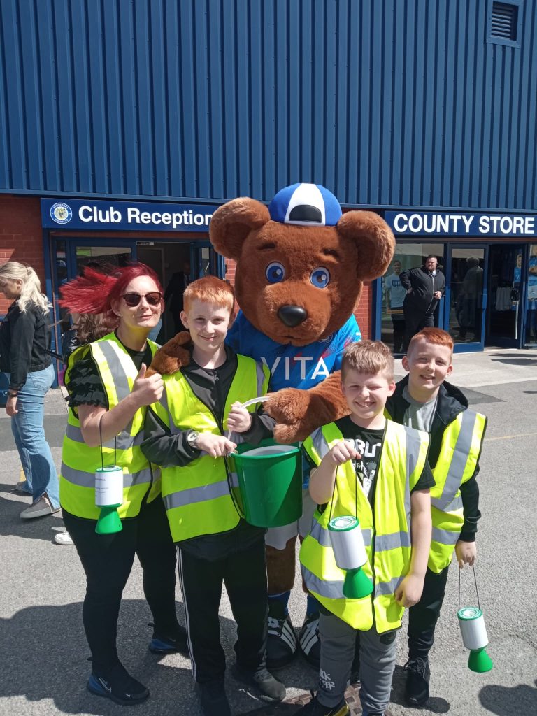 Emma and boys from Paramount ABC stand with Vernon Bear collecting tins at the ready