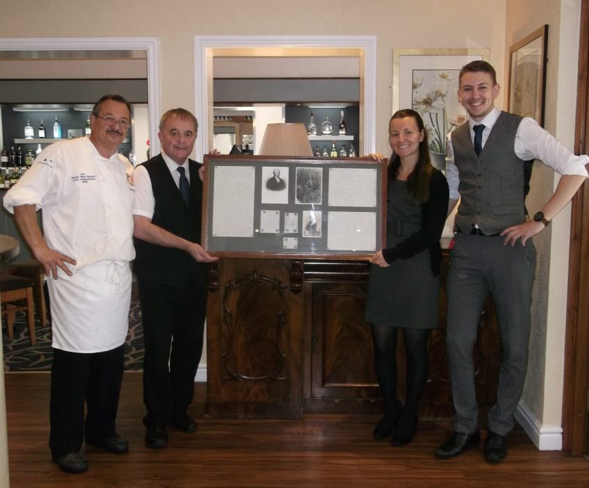 Staff and chef hold a large framed collection of old pictures and research