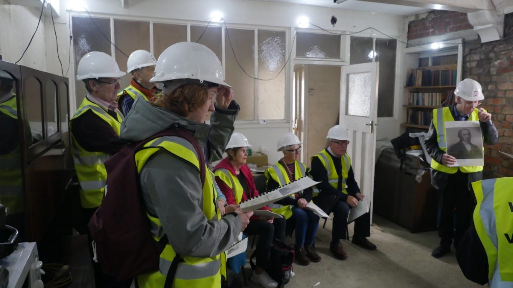 Visitors in hard hats and hi-viz study a handout with old pictures on it to accompany the talk