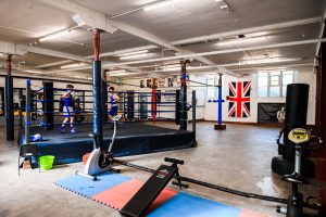 A bright view of the basement gym area with just boys in blue practising in the ring