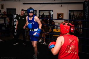 A boy from Paramount in blue weighs up a boy from Holmes Chapel boxing club in red in the ring